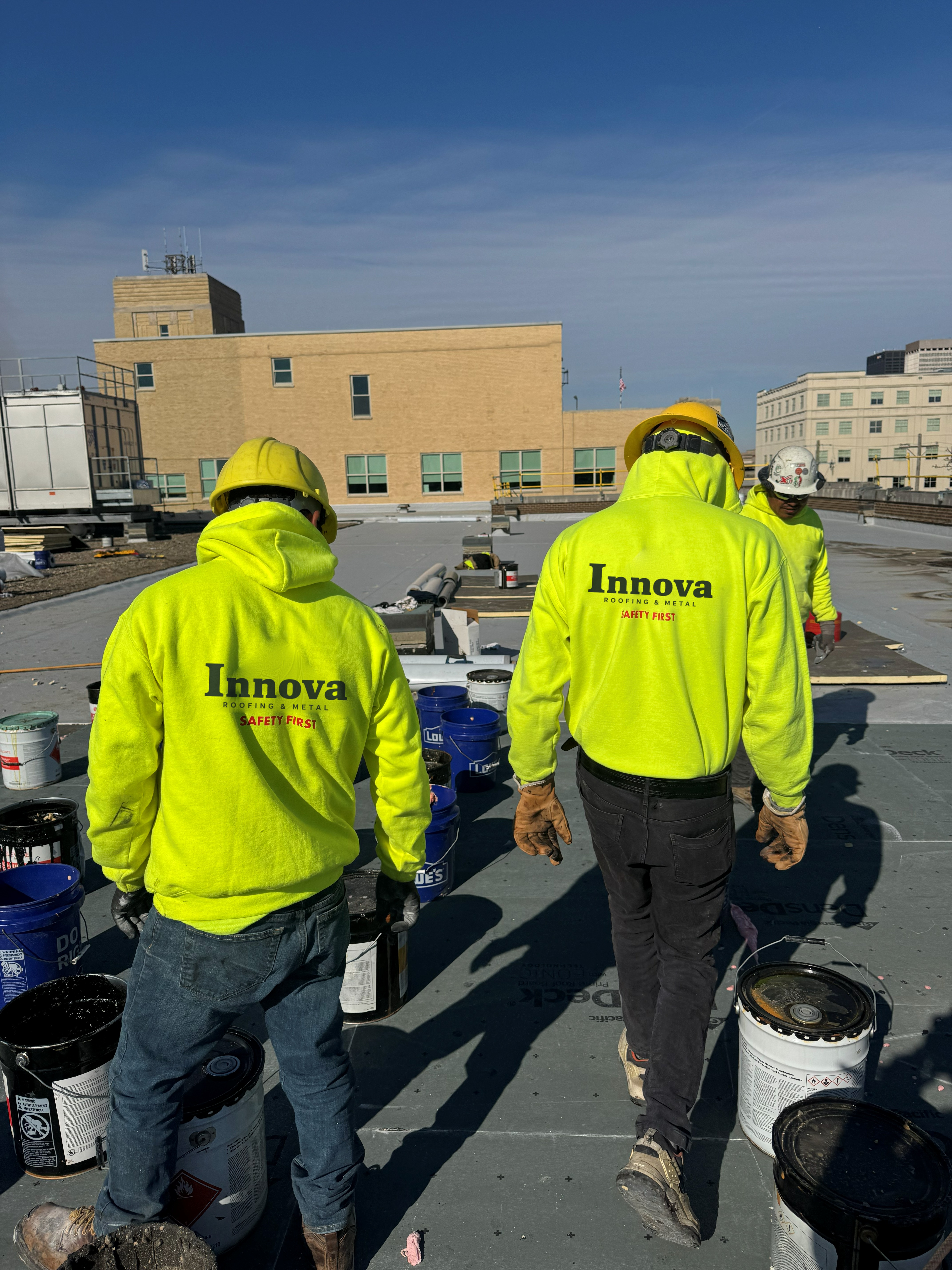 Innova roofing crew wearing bright yellow branded hoodies and hard hats on a commercial roof.
