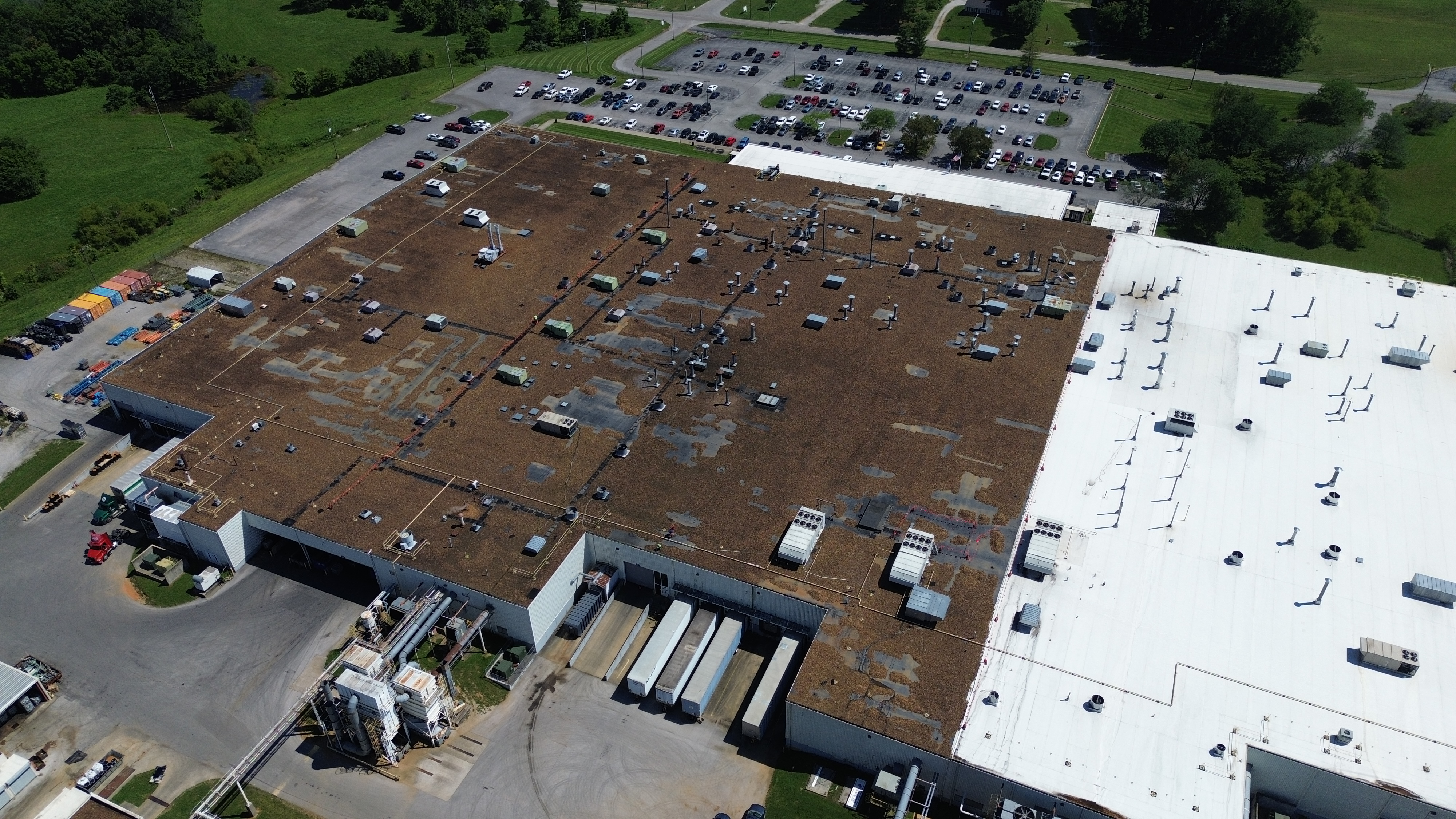 Aerial view of a large industrial building with a gravel-surfaced main roof beside sections of white roofing.