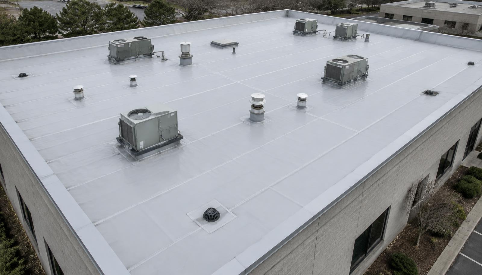 Aerial view of a light gray single-ply PVC membrane roof with rooftop HVAC units, vents, and drains (illustrative image)