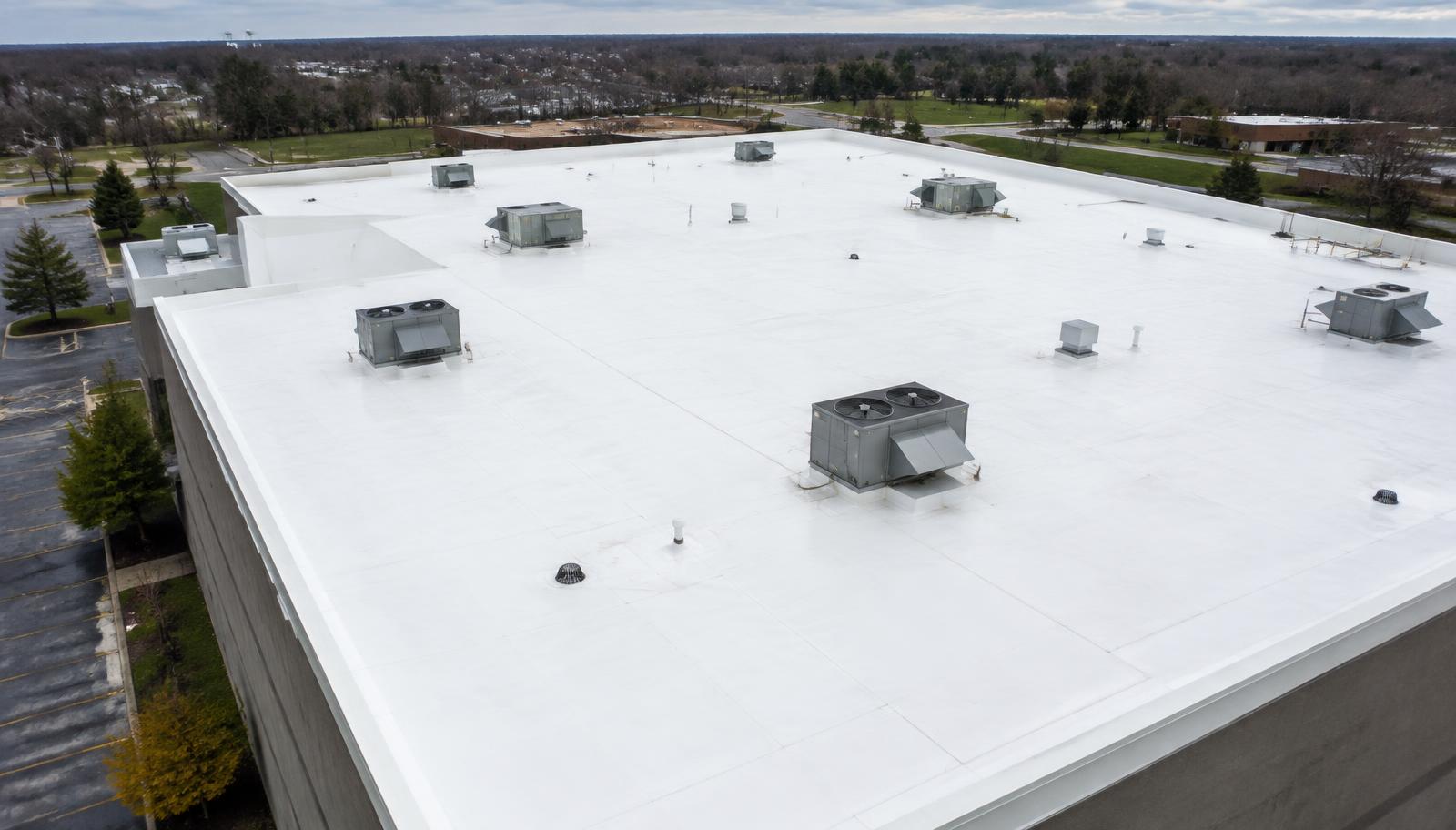 Aerial view of a white single-ply TPO membrane roof with rooftop HVAC units and drains (illustrative image)